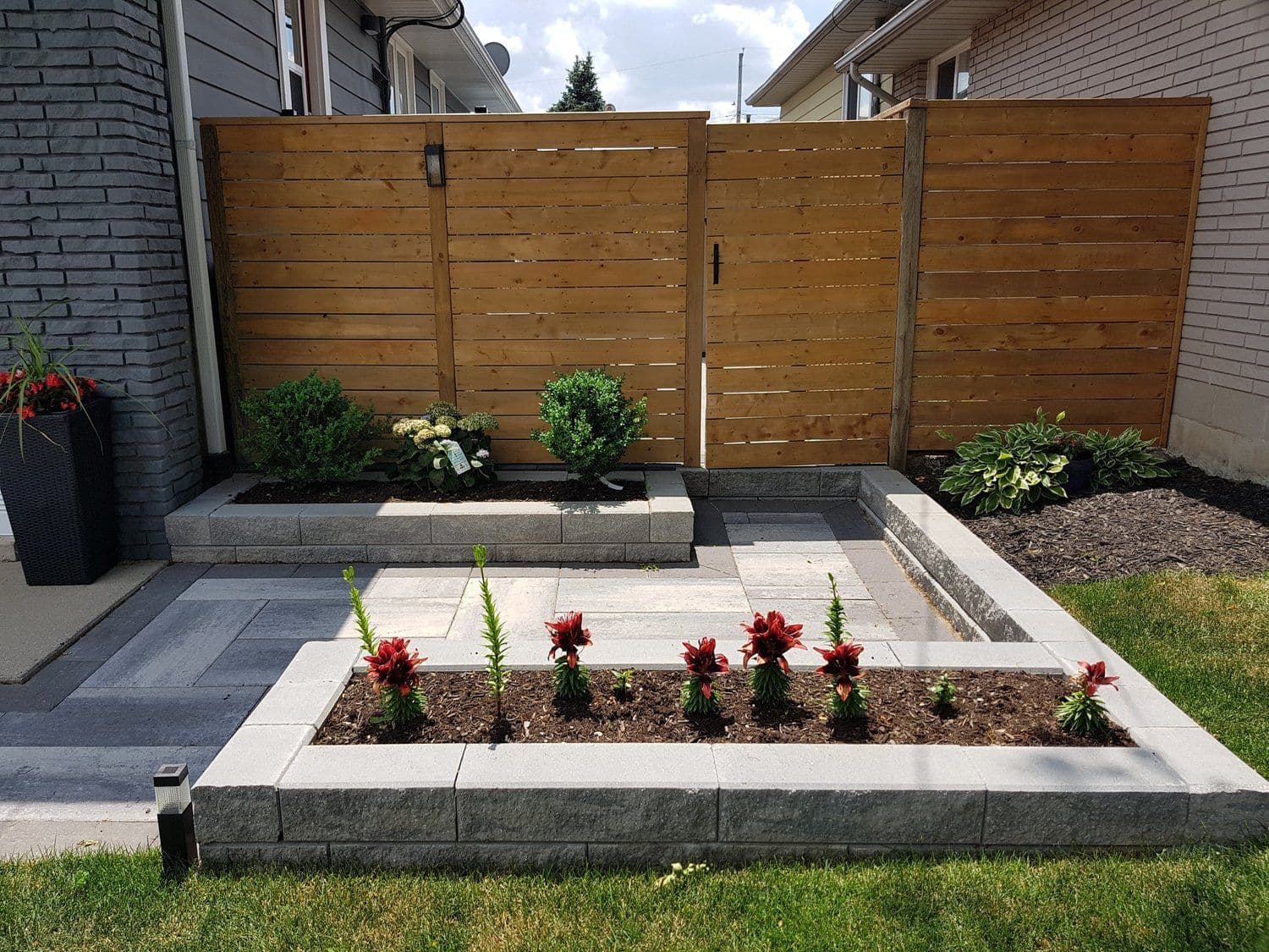 Paver patio with raised garden beds and red flowering plants, wood privacy fence