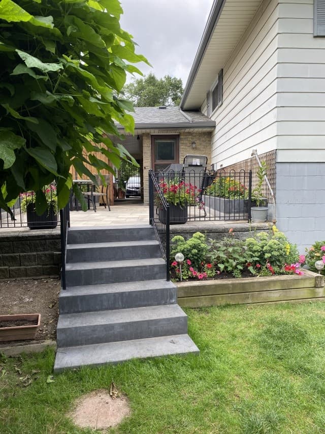 Stone front steps and paver patio leading to covered porch with planters
